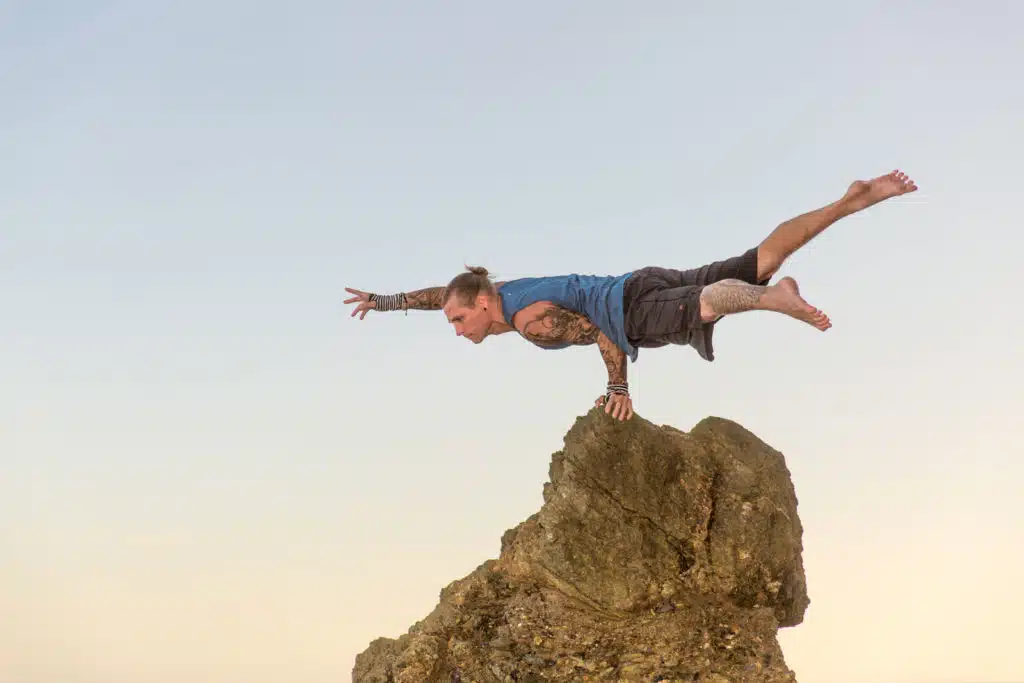 Coach Kyle Weiger doing a One Hand Peacock yoga pose on the top of a rock