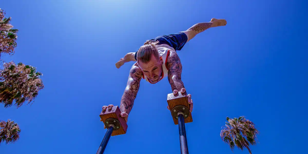 Coach Kyle Weiger doing a handstand on an H-shape Canes Trainer underneath the bright blue sky