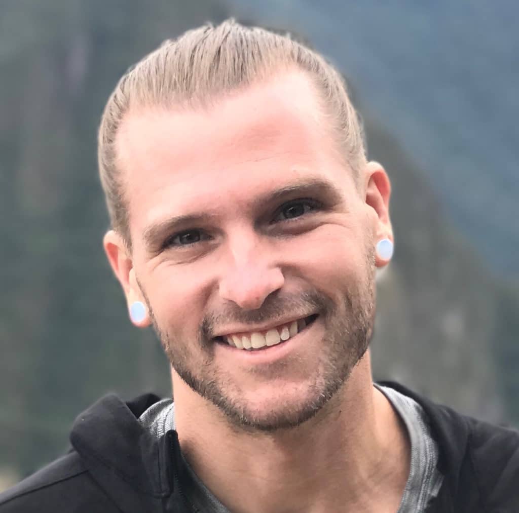 Headshot of Handstand Trainer Coach Kyle Weiger Smiling Tied Hair Man Bun With Blue Earrings