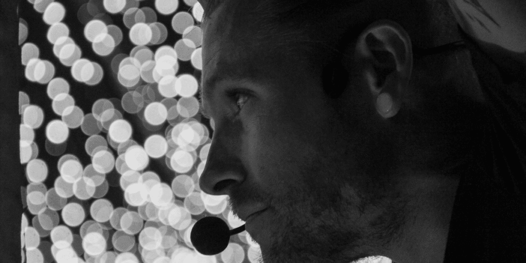 Black and white semi silhouette headshot of handstand coach Kyle Weiger wearing earhook mic with bokeh light background