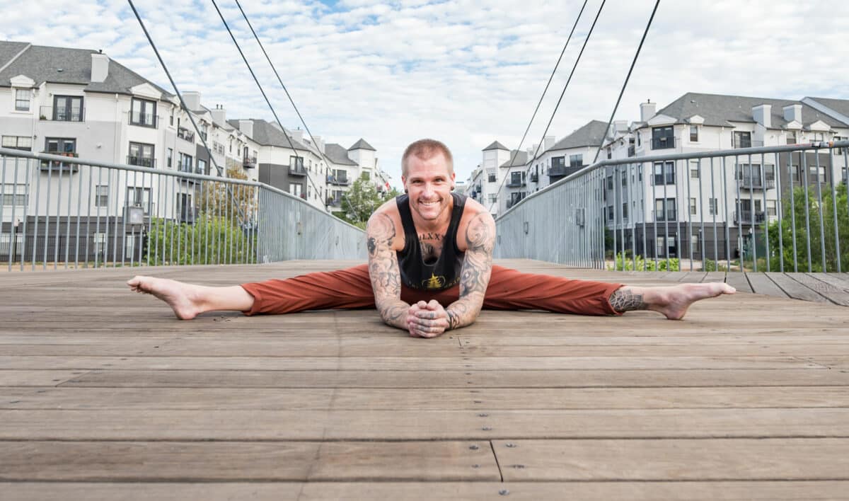 Smiling handstand coach Kyle Weiger front view splitting on wooden floor with houses in the background