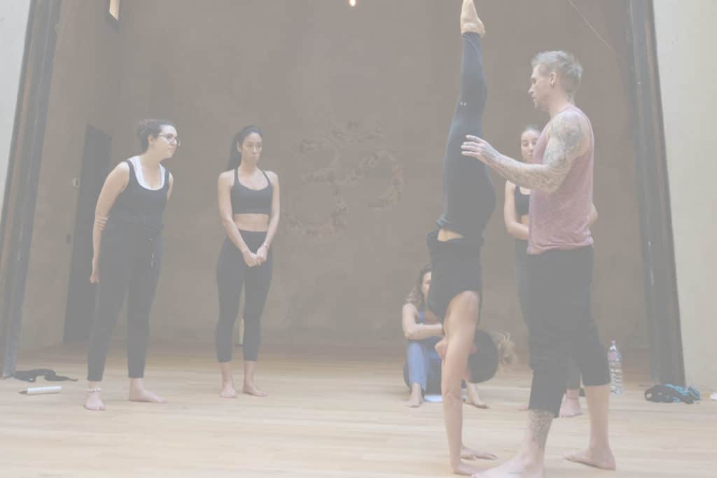 Instructor Kyle Weiger assists girl students in the gym 4 essential handstand elements course with white filter