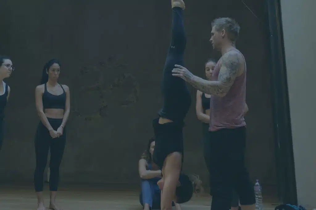 Instructor Kyle Weiger assists a girl student in the gym while others are watching with a dark filter