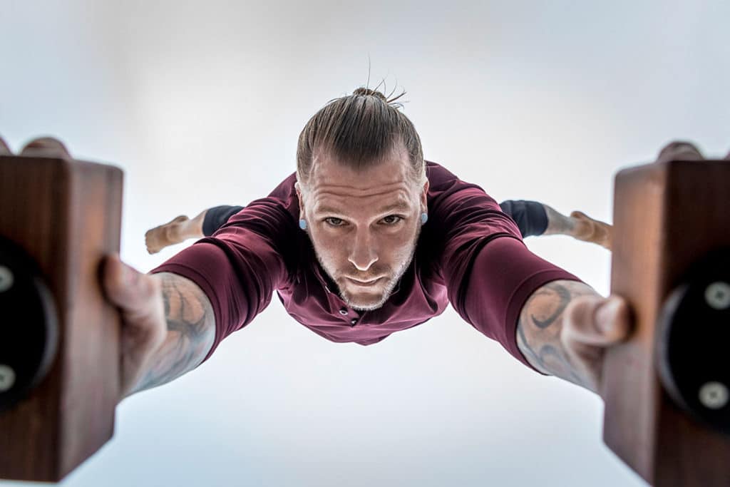Coach Kyle Weiger doing a handstand on an H-shape Canes Trainer with a camera view underneath with cloudy sky