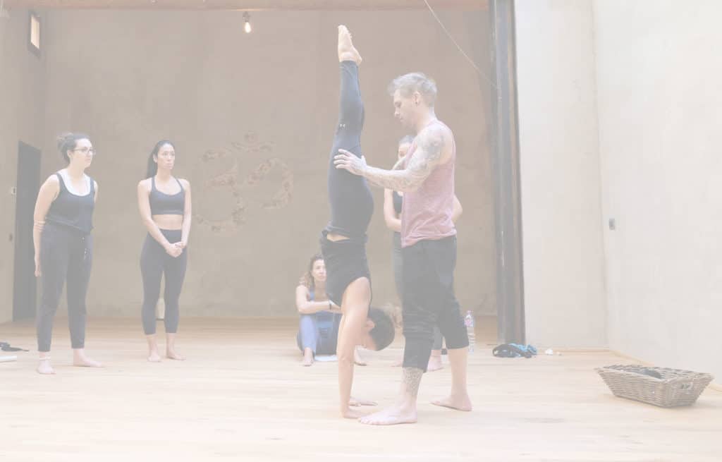Instructor Kyle Weiger assists girl students in the gym 4 essential handstand elements course with white filter