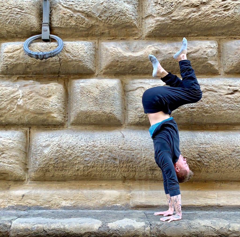 Coach Kyle Weiger wearing a dark cyan long sleeve doing a handstand near a wall