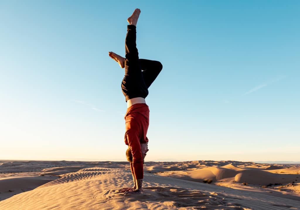 Side view of Coach Kyle Weiger handstanding with one leg down outdoors high altitude background while the sun is setting