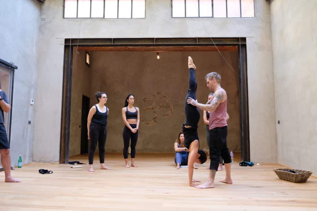 Instructor Kyle Weiger assists girl student in the gym while others are watching 4 essential handstand elements course