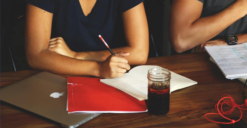 Two students sitting in front and leaning on the side of the table with macbook notebooks and drinks