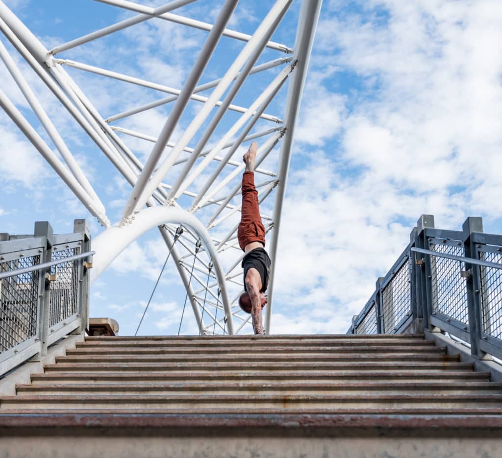 Side view of coach Kyle Weiger handstanding above stairs of Denver Colorado Highland Bridge