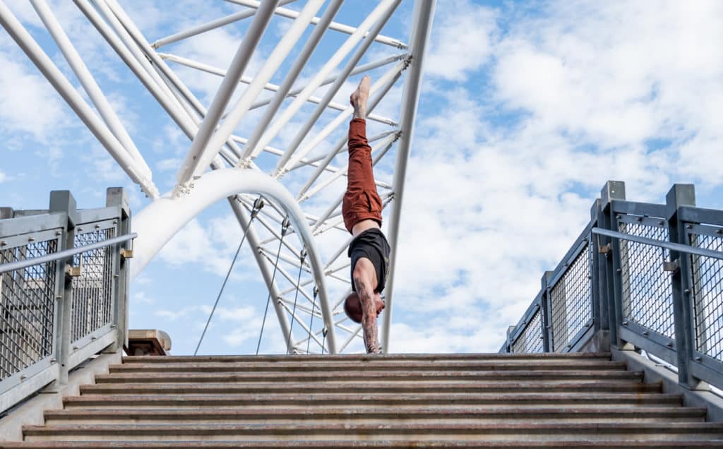 Side view of coach Kyle Weiger handstanding above stairs of Denver Colorado Highland Bridge