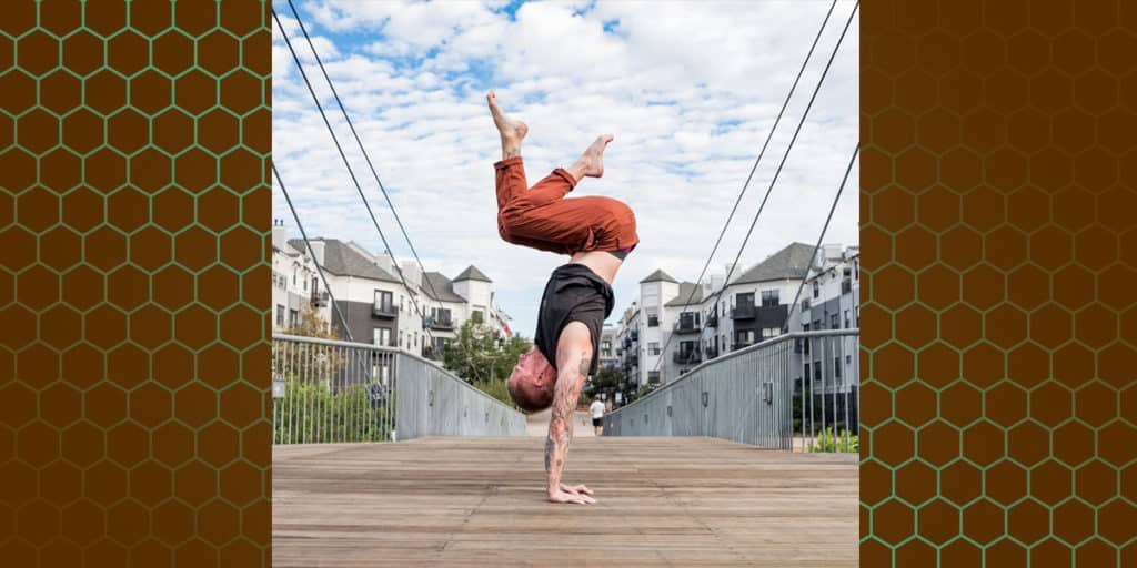 Side view of coach Kyle Weiger handstanding tuck on the wooden floor with houses in the background