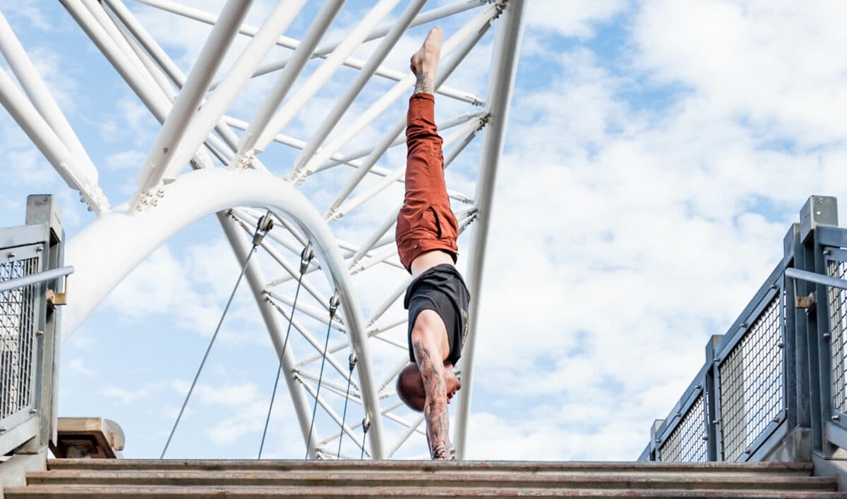 Side view of coach Kyle Weiger handstanding above stairs of Denver Colorado Highland Bridge
