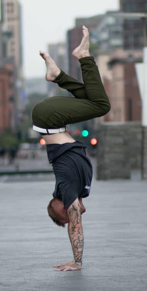 Coach Kyle Weiger doing a handstand side view at the street with blurred buildings in the background