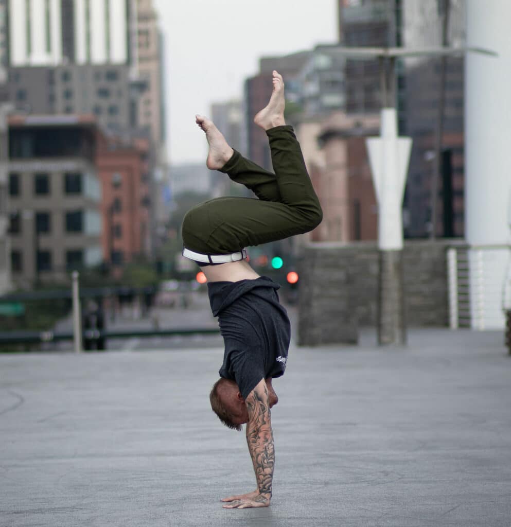 Coach Kyle Weiger doing a handstand side view at the street with blurred buildings in the background