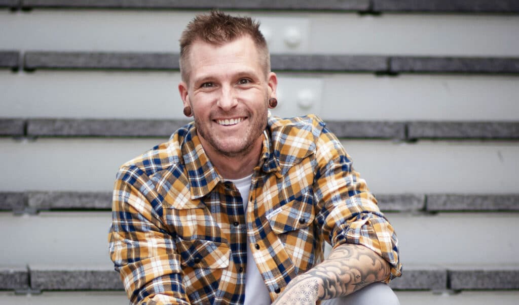 Smiling handstand coach Kyle Weiger wearing checkered polo shirt casual street photo with stripe background