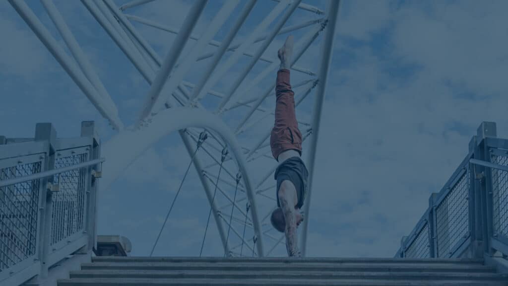 Side view of coach Kyle Weiger handstanding above stairs of Denver Colorado Highland Bridge with teal filter