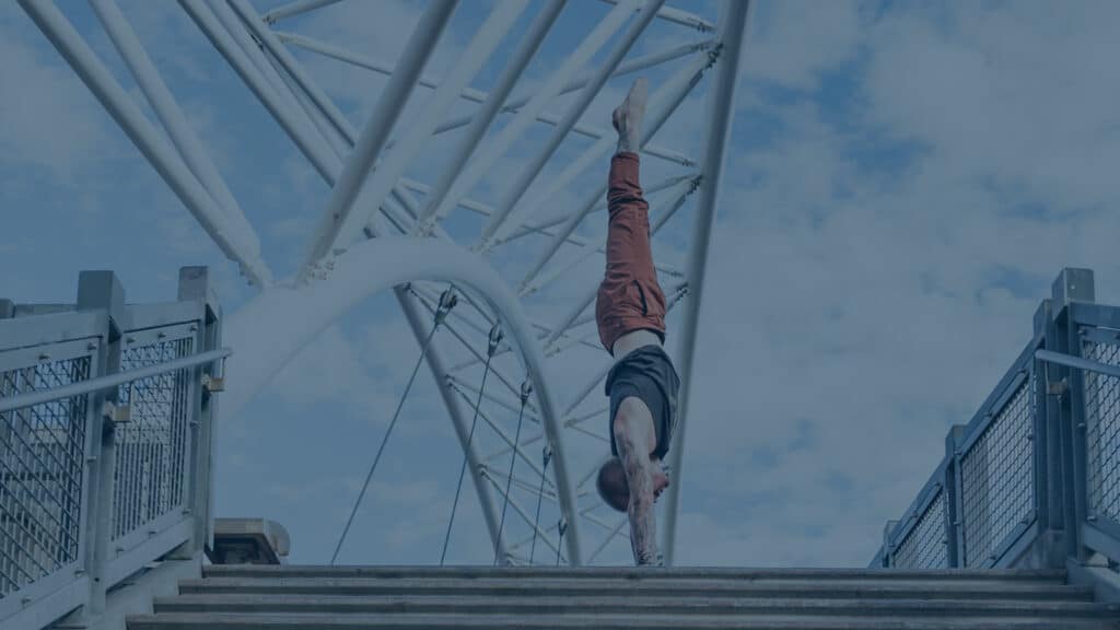 Side view of coach Kyle Weiger handstanding above stairs of Denver Colorado Highland Bridge with teal filter
