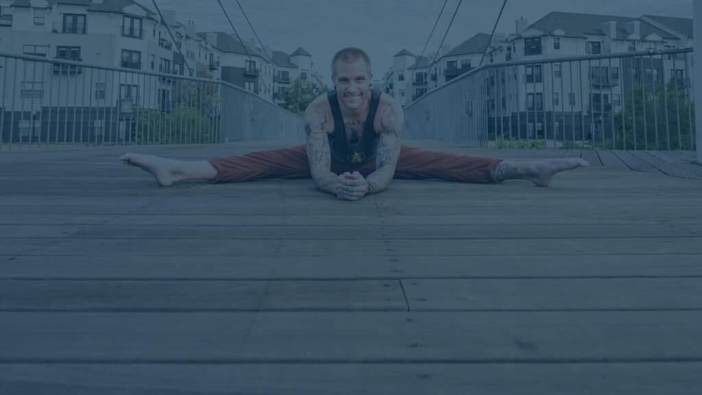 Smiling handstand coach Kyle Weiger front view splitting on wooden floor with houses on the background and teal filter