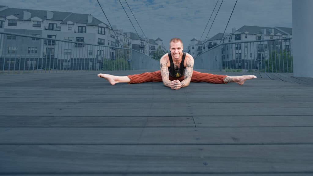 Smiling handstand coach Kyle Weiger front view splitting on the floor with a dark teal background