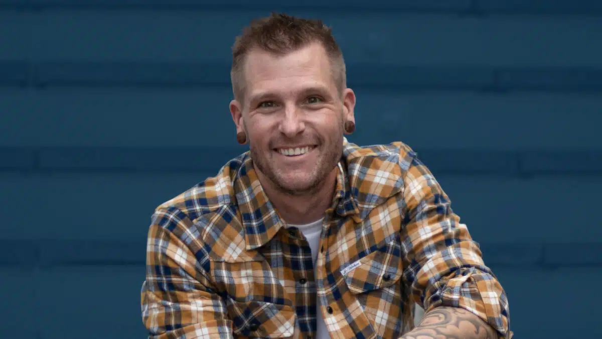 Smiling handstand coach Kyle Weiger wearing checkered polo shirt casual street photo with dark teal stripe background