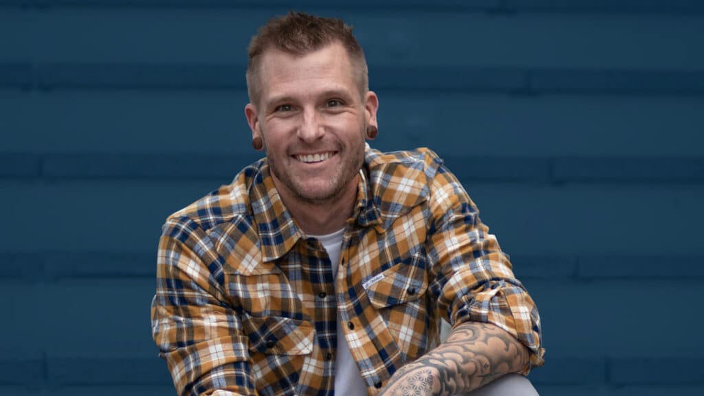 Smiling handstand coach Kyle Weiger wearing checkered polo shirt casual street photo with dark teal stripe background