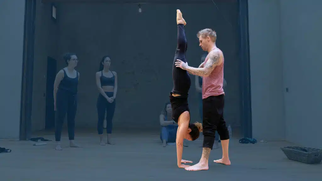 Instructor Kyle Weiger assists girl students in the gym 4 essential handstand elements course with dark teal background