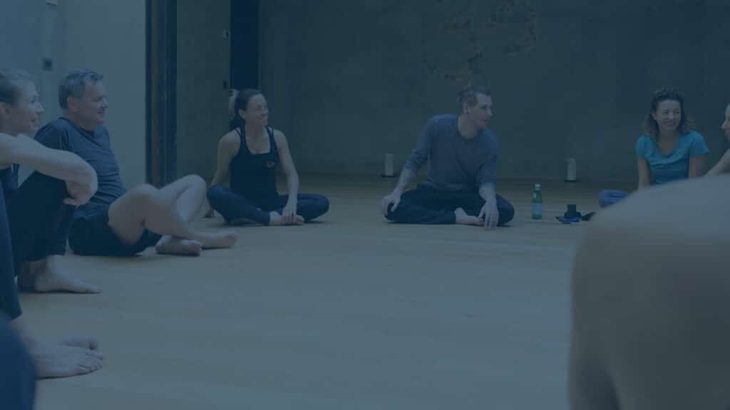 Handstand coach Kyle Weiger sits in circle with students in gym photo with teal filter
